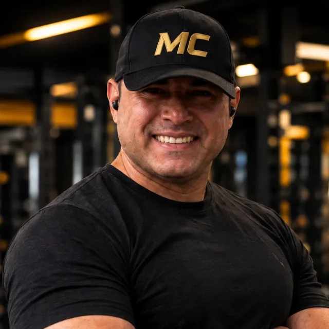Márcio Carvalho sorrindo, de boné MC, na academia